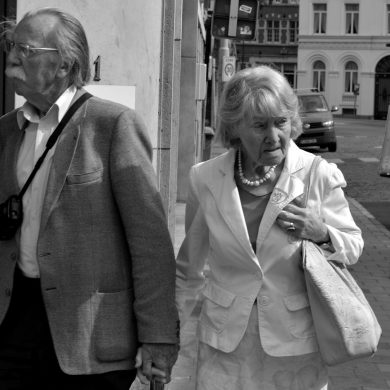 Twee oude mensen lopen hand in hand over straat