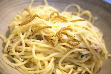 Close-up bord met pasta carbonara en meelwormen