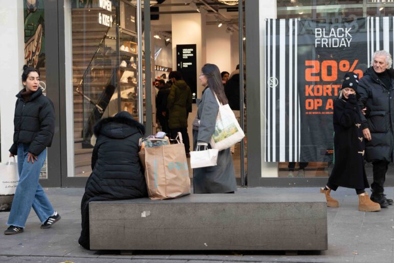 Mensen wandelen uit winkel met korting. Vrouw zit op de bank met winkelzakken.