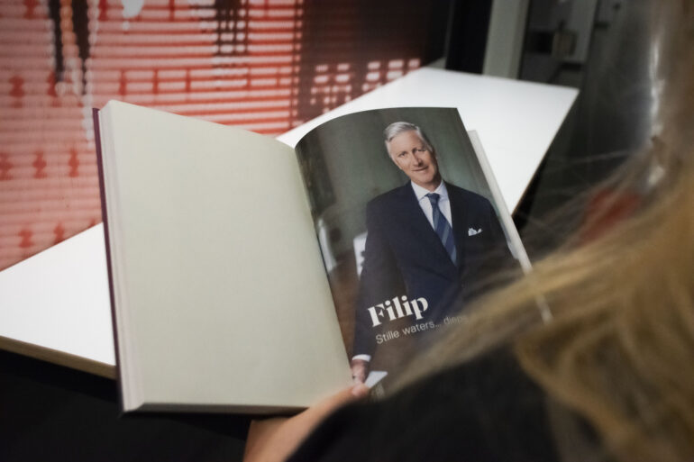 Je kijkt mee over de schouder van een vrouw die een boek leest over koning Filip.