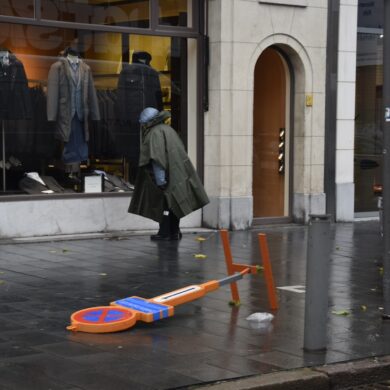 Een vrouw in regenjas passeert een omgevallen verkeersbord.