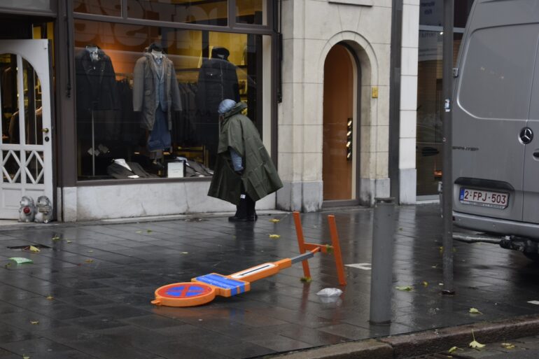 Een vrouw in regenjas passeert een omgevallen verkeersbord.