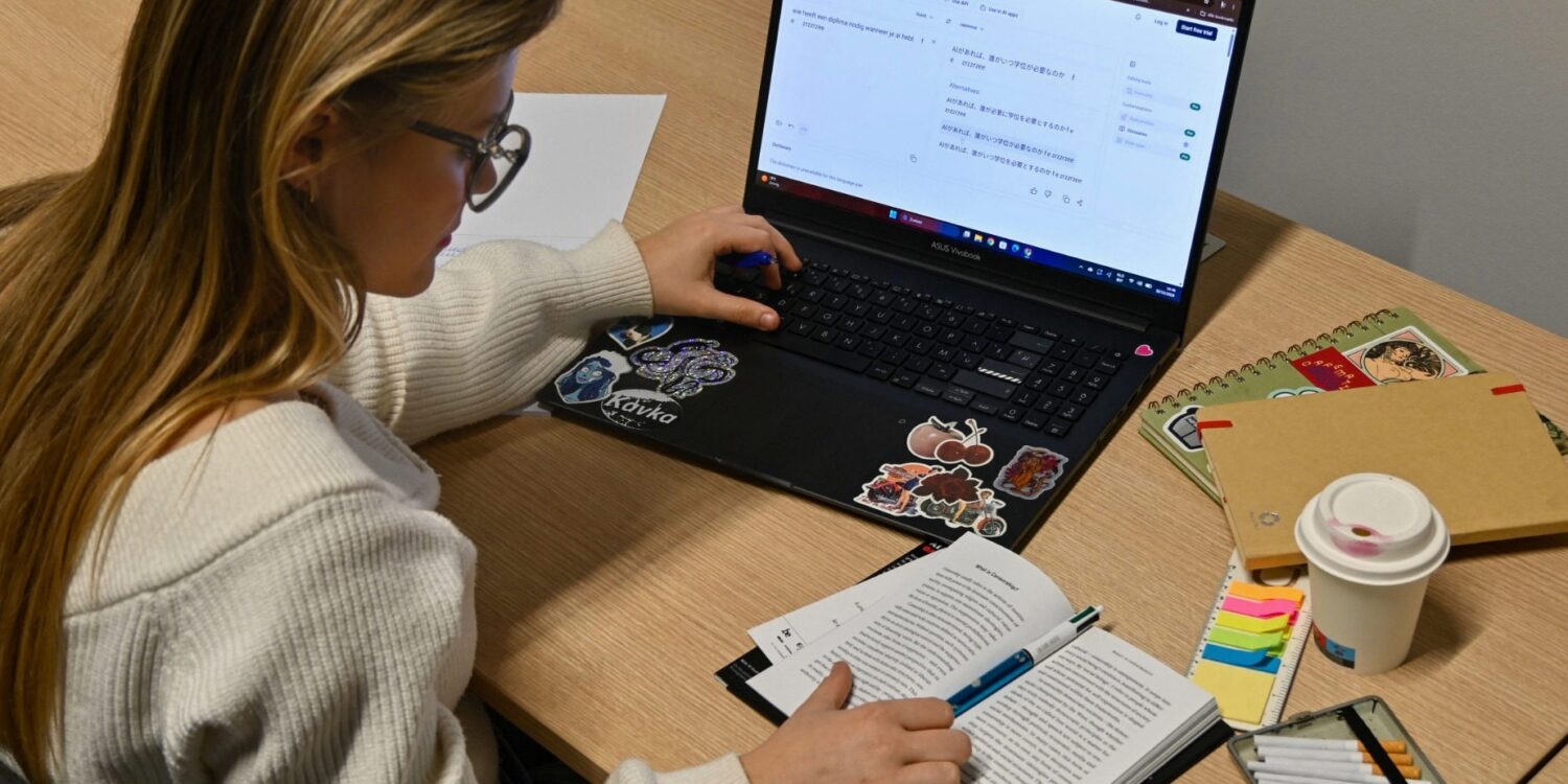 Een vertaler aan het werk met een open boek en een laptop waarop DeepL een tekst naar het Japans vertaalt.